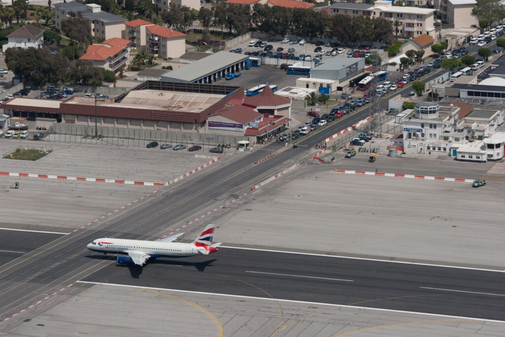 Gibraltar Blick von oben auf die Landebahn mit Flugzeug, die auch gleichzeitig als Strasse genutzt wird. Darauf weisen zahlreiche Autos in der Warteschlange hin